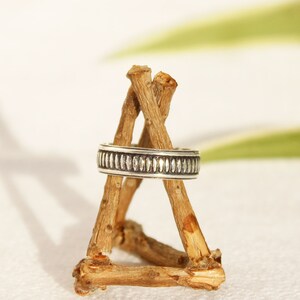 May include: A silver ring with a textured band sits on a wooden display stand. The ring is simple and elegant.