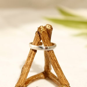 May include: A silver ring displayed on a wooden ring holder. The holder is made of three pieces of wood arranged in a triangular shape.
