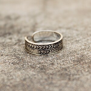 May include: Silver toe ring with a decorative design of two rows of small leaves.