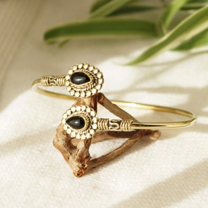 Peut inclure: Un bracelet jonc en or avec deux accents de pierres précieuses noires. Le bracelet est décoré de petites perles et est ouvert d'un côté.