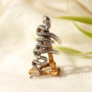 Peut inclure: Une bague en argent en forme de serpent enroulé. La bague est présentée sur un support en bois.
