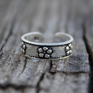 May include: Silver toe ring with a floral design. The ring is made of a smooth metal and has a polished finish.