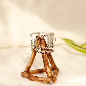 May include: Silver ring with an intricate design and a clear stone. The ring is displayed on a wooden stand.
