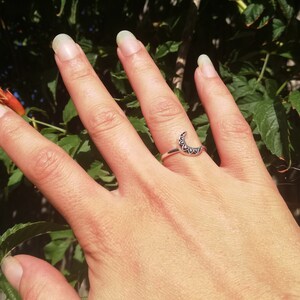 May include: A silver ring with a crescent moon design. The moon is decorated with small, intricate details.