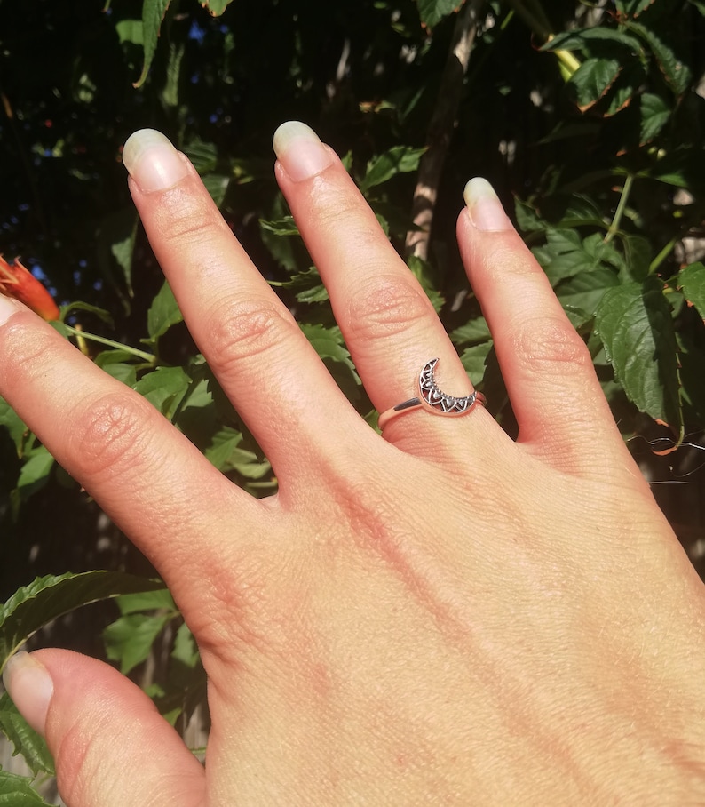 May include: A silver ring with a crescent moon design. The moon is decorated with small, intricate details.