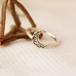 May include: A silver ring with a crescent moon design. The moon is detailed with a mandala pattern.