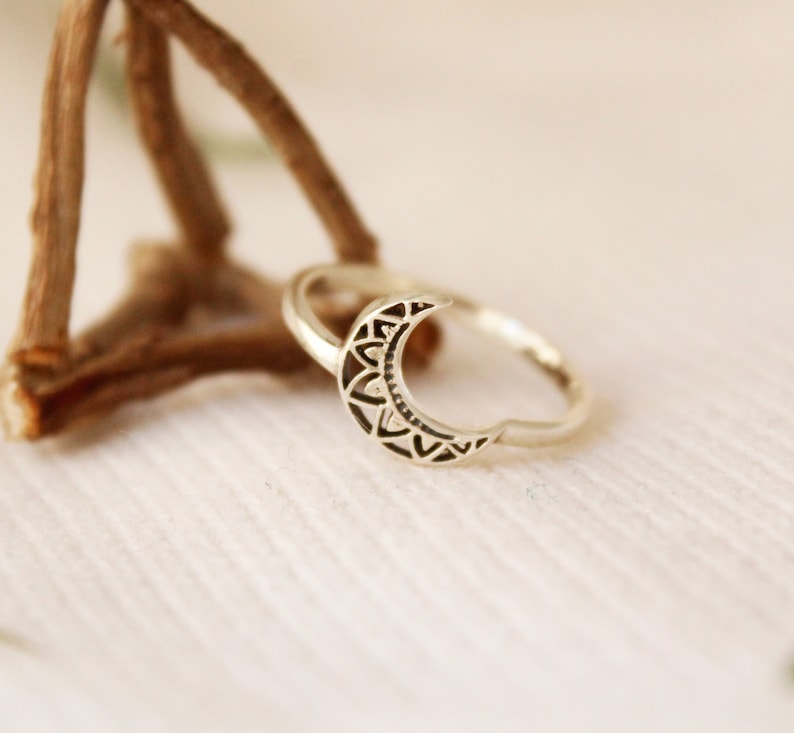 May include: A silver ring with a crescent moon design. The moon is detailed with a mandala pattern.
