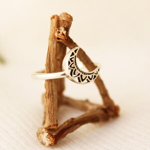 May include: A silver ring with a crescent moon design. The moon is decorated with a detailed mandala pattern.
