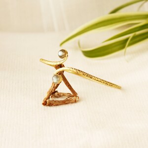 May include: A gold-toned bracelet with two iridescent stones. The bracelet is twisted and has a textured finish.