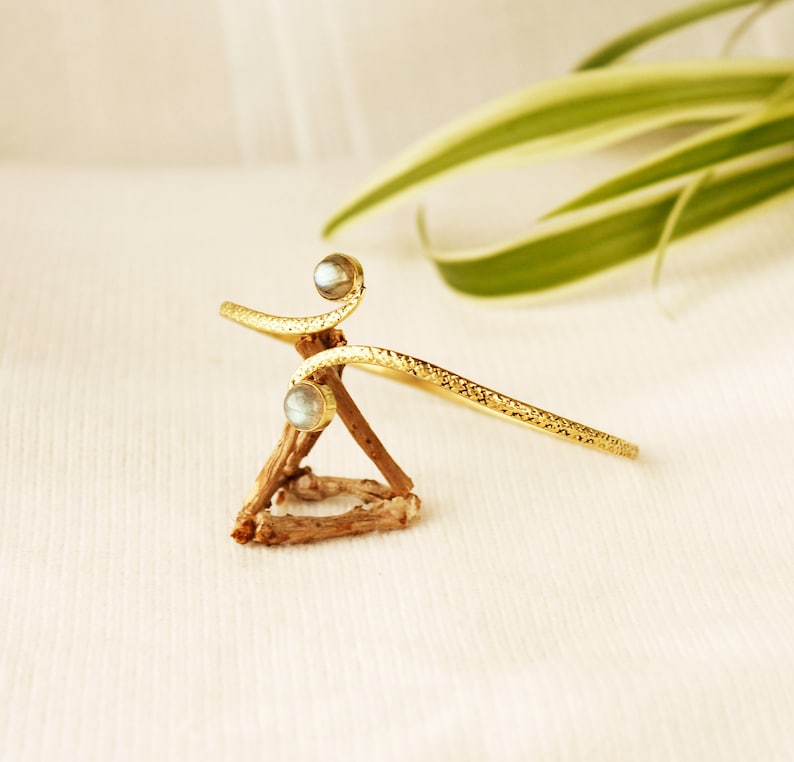 May include: A gold-toned bracelet with two iridescent stones. The bracelet is twisted and has a textured finish.