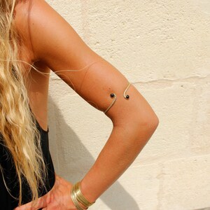 May include: A gold arm cuff with two black beads. The cuff is worn on the upper arm.
