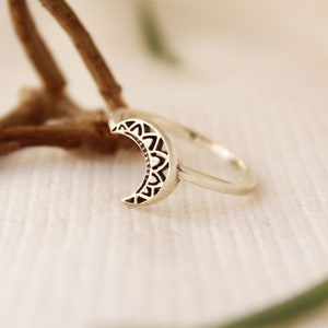 May include: A silver ring with a crescent moon design. The moon is detailed with a mandala pattern.