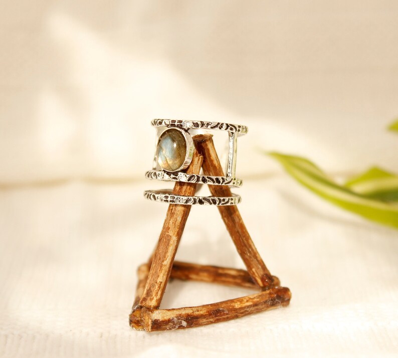 May include: A silver ring with a round, iridescent gemstone set in a triple band design. The ring is displayed on a wooden stand.