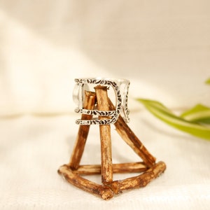 May include: Silver ring with an intricate design, displayed on a wooden stand.