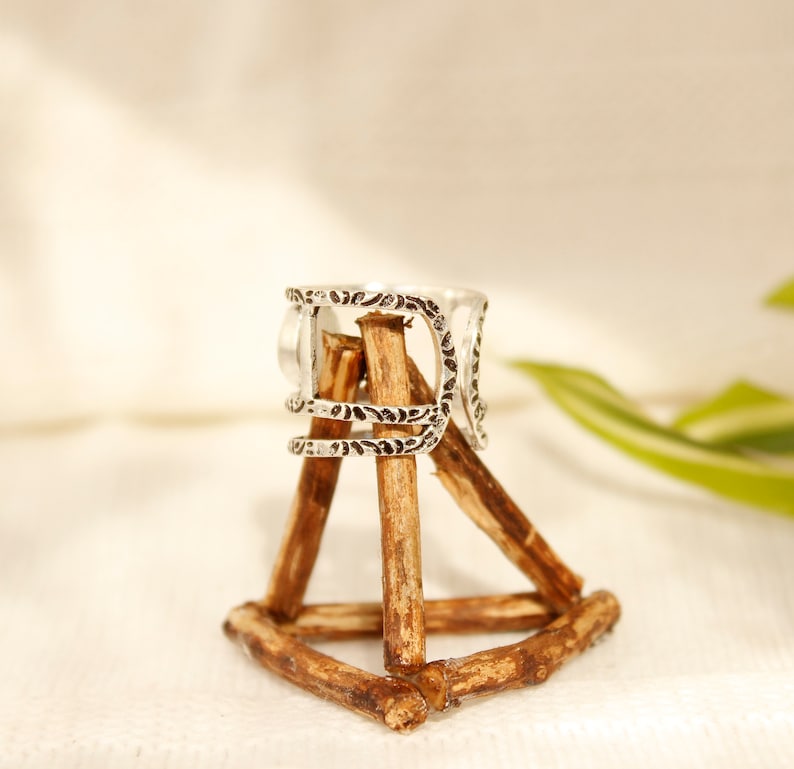 May include: Silver ring with an intricate design, displayed on a wooden stand.
