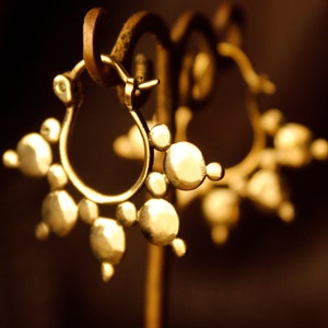 May include: A pair of gold hoop earrings with a cluster of small, round, textured gold beads. The earrings are hanging from a display stand.