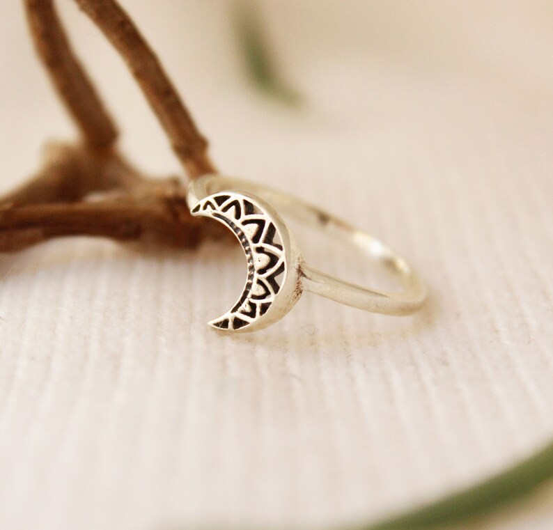 May include: A silver ring with a crescent moon design. The moon is detailed with a mandala pattern.