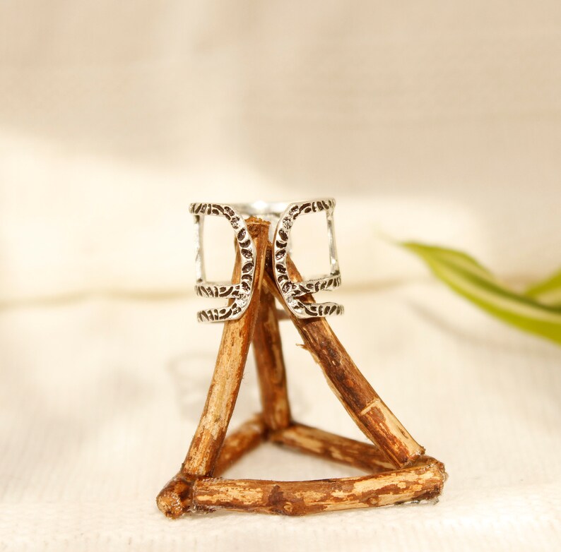 May include: Silver ring with an intricate design, displayed on a wooden stand. The ring has a unique openwork design with multiple layers.