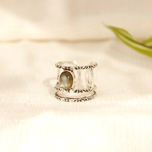 May include: Silver ring with a textured band and a single oval-shaped gemstone in the center.