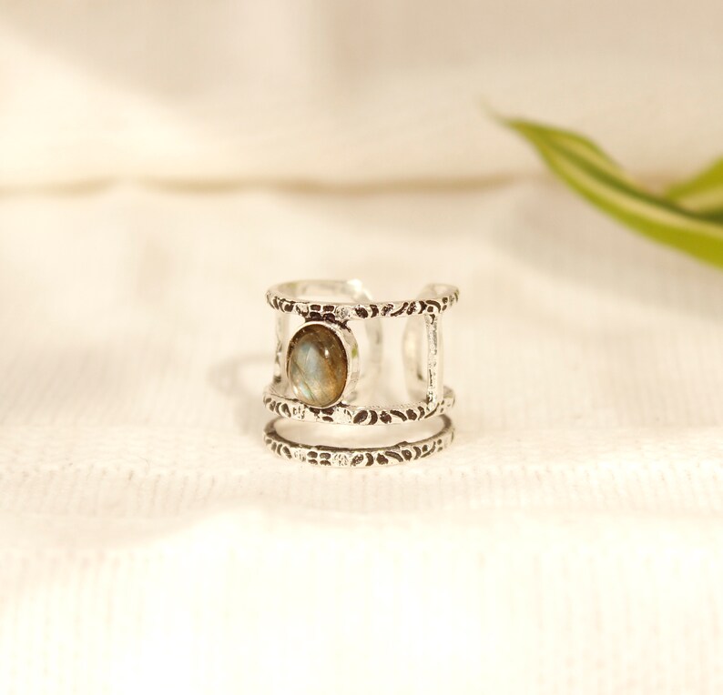 May include: Silver ring with a textured band and a single oval-shaped gemstone in the center.