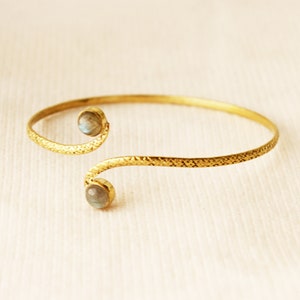 May include: A gold bracelet with a textured finish and two round, iridescent stones.