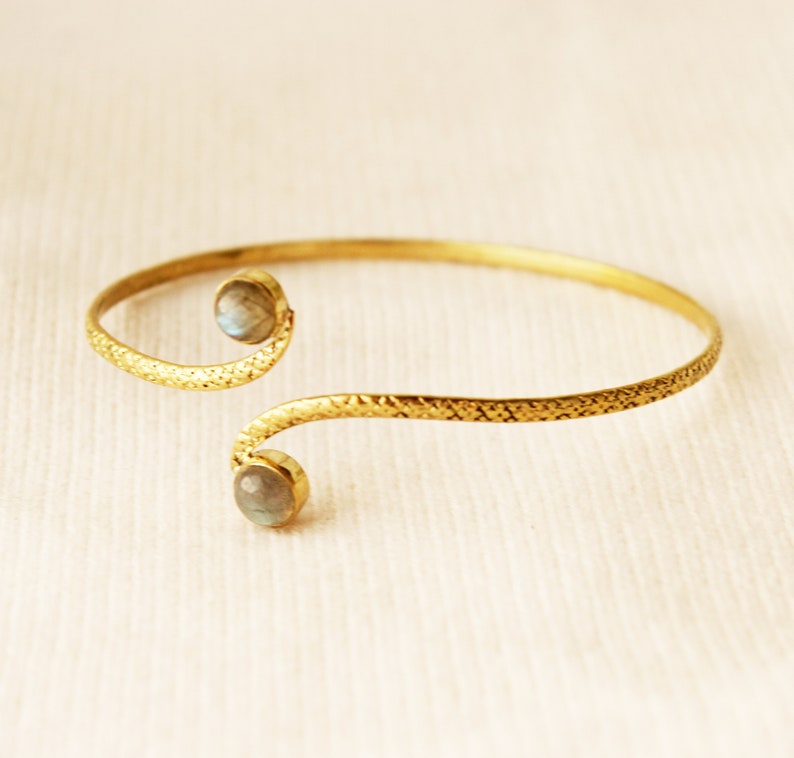 May include: A gold bracelet with a textured finish and two round, iridescent stones.