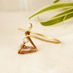 May include: A gold-toned bracelet with a textured design and two white moonstone accents.