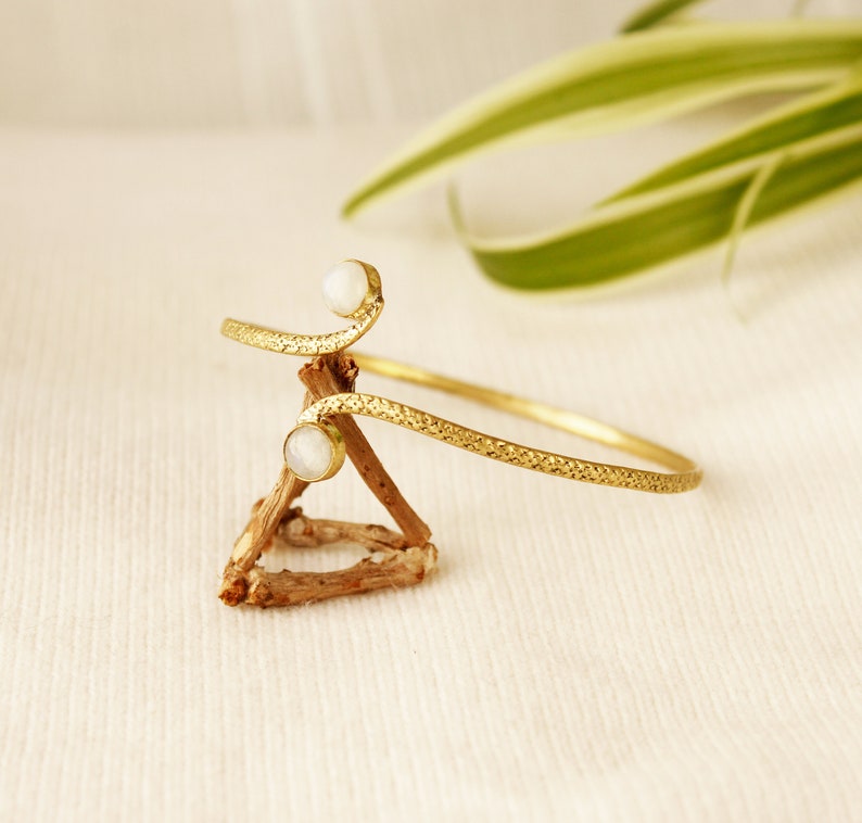 May include: A gold-toned bracelet with a textured design and two white moonstone accents.