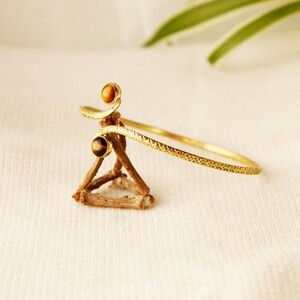 May include: A gold bangle bracelet with a textured finish and two tiger's eye stones.