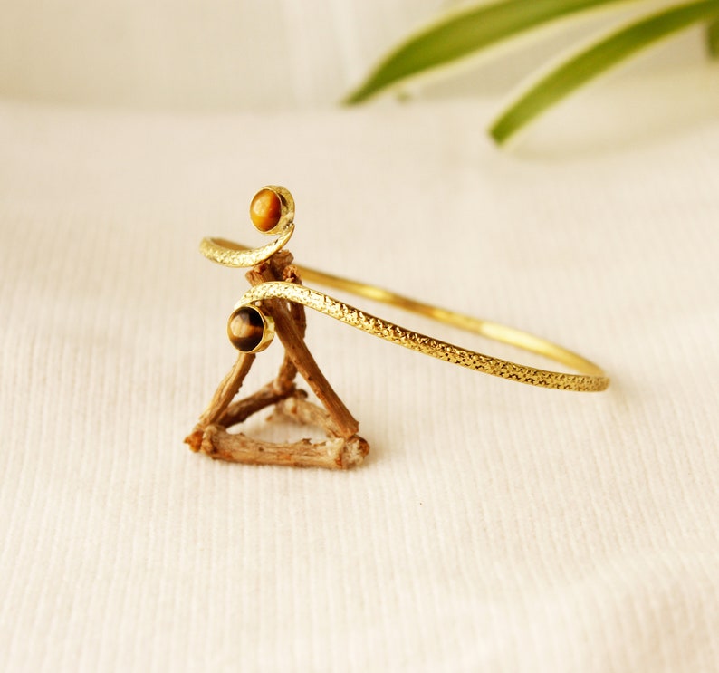 May include: A gold bangle bracelet with a textured finish and two tiger's eye stones.