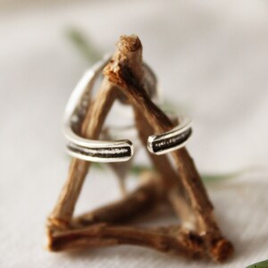 May include: A silver ring with a textured band, displayed on a wooden stand.