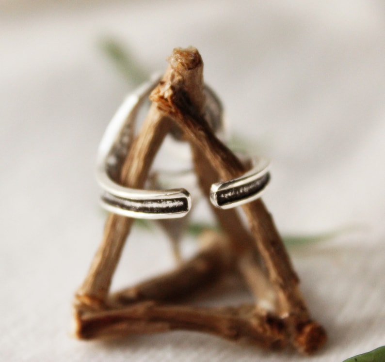 May include: A silver ring with a textured band, displayed on a wooden stand.