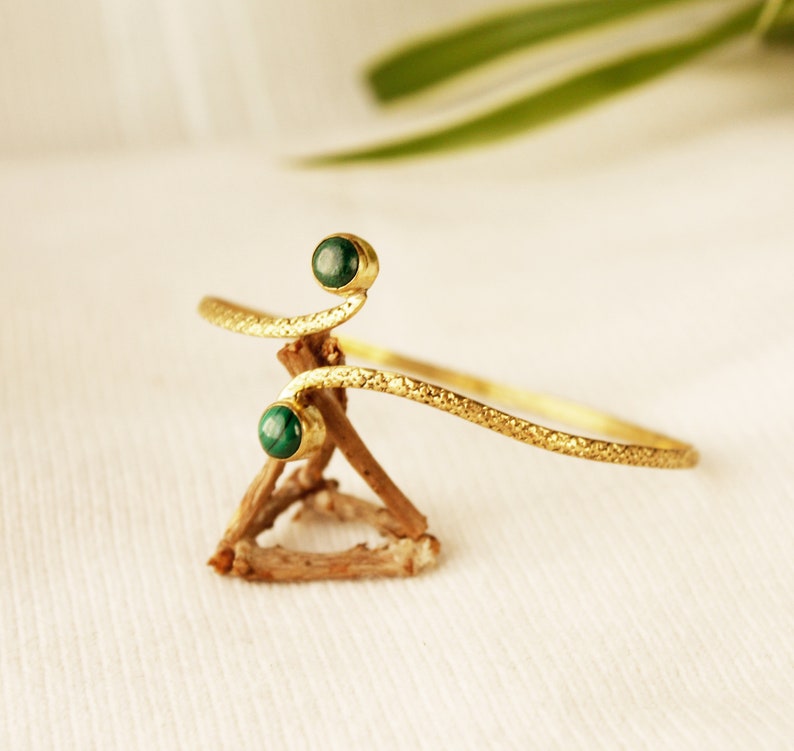 May include: A gold-toned bracelet with a textured finish and two green gemstone accents.