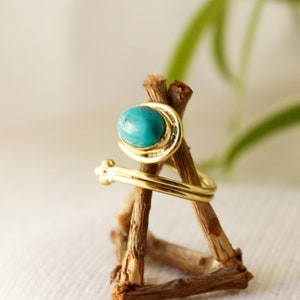 K&ouml;nnte beinhalten: Ein goldener Ring mit einem t&uuml;rkisfarbenen Stein, der in einem gedrehten Band gefasst ist. Der Ring wird auf einem Holzst&auml;nder pr&auml;sentiert.