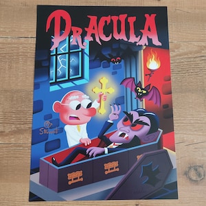 May include: A colorful Dracula-themed print. The word "Dracula" is in large red letters at the top. The illustration depicts a cartoon vampire in a coffin, facing a character holding a cross. Bats and a torch are also in the image.