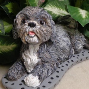 May include: A gray and white ceramic figurine of a Shih Tzu dog lying down on a gray and black polka dot base.