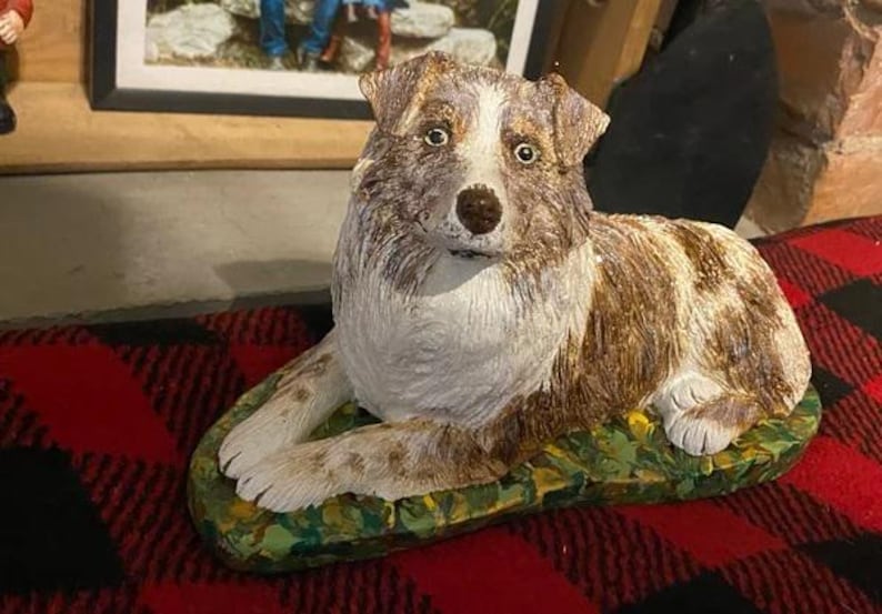 May include: A ceramic figurine of a brown and white dog with blue eyes, sitting on a green and yellow base. The dog is lying down with its head tilted to the side.