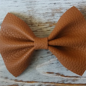 May include: A brown leather bow tie with a pointed shape. The bow tie is made of a textured leather material.