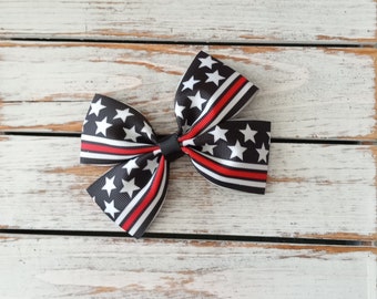 May include: A black and white bow with red stripes and white stars. The bow is made of ribbon and has a black center.
