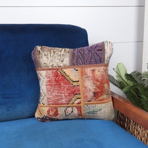 May include: A colorful patchwork throw pillow with a square shape and a variety of colors and patterns, including red, orange, yellow, green, blue, and purple. The pillow is sitting on a blue velvet chair.