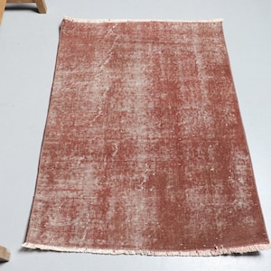 Op de afbeelding: Een vintage-stijl tapijt met een vervaagde, verweerde look. Het tapijt is een stoffige roze kleur met een subtiel patroon. Het heeft een gefranst randje.