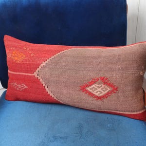 May include: A red and brown patterned cushion with a geometric design. The cushion is on a blue velvet chair.