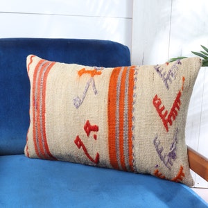 May include: A decorative throw pillow with a beige background and colorful geometric patterns in orange, purple, and red. The pillow is sitting on a blue velvet chair.