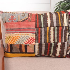 May include: A rectangular cushion with a patchwork design. The cushion features a mix of colours including red, orange, brown, and grey. The design includes stripes and geometric patterns, adding a unique touch to home decor.