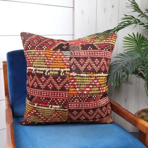 May include: A colorful, patterned throw pillow with a geometric design in shades of red, orange, brown, and green. The pillow is sitting on a blue velvet chair.