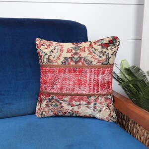 May include: A red, white, and blue patterned throw pillow with a brown leather trim. The pillow is sitting on a blue velvet couch.