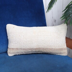 May include: A white and beige striped throw pillow with a soft, textured fabric. The pillow is sitting on a blue velvet sofa.