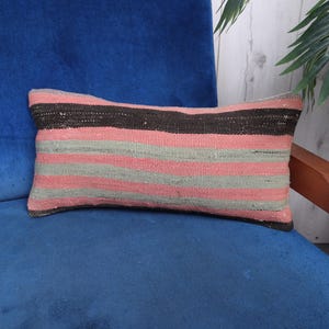 May include: A long, rectangular pillow with a striped pattern in shades of pink, gray, and brown. The pillow is made of a woven fabric and has a soft, textured surface.