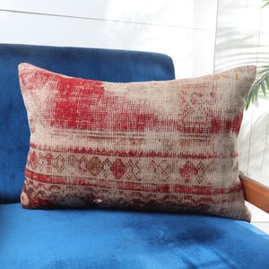 Puede incluir: Un cojín de tiro rojo y crema con textura tejida se sienta en un sillón de terciopelo azul.