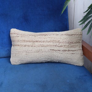 May include: A white and brown striped throw pillow with a woven texture. The pillow is sitting on a blue couch.